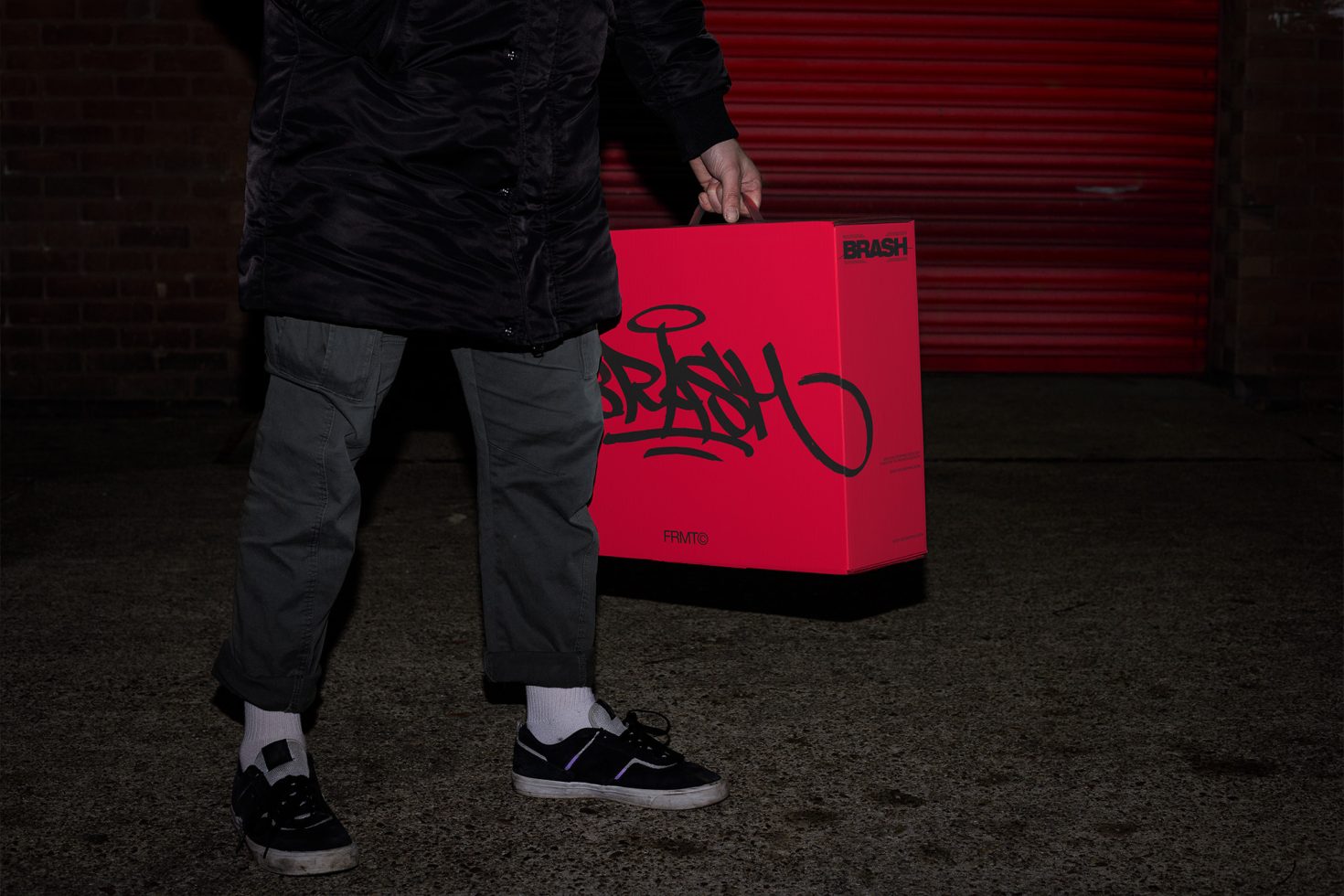 Person in urban setting holding a bold red product box with dynamic black script font, ideal for packaging mockup designs for designers.